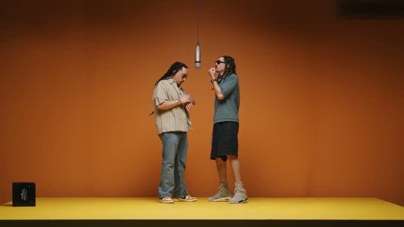 Two performers at a hanging microphone in a matte-orange studio, a Hotel Lobby video recast with AI